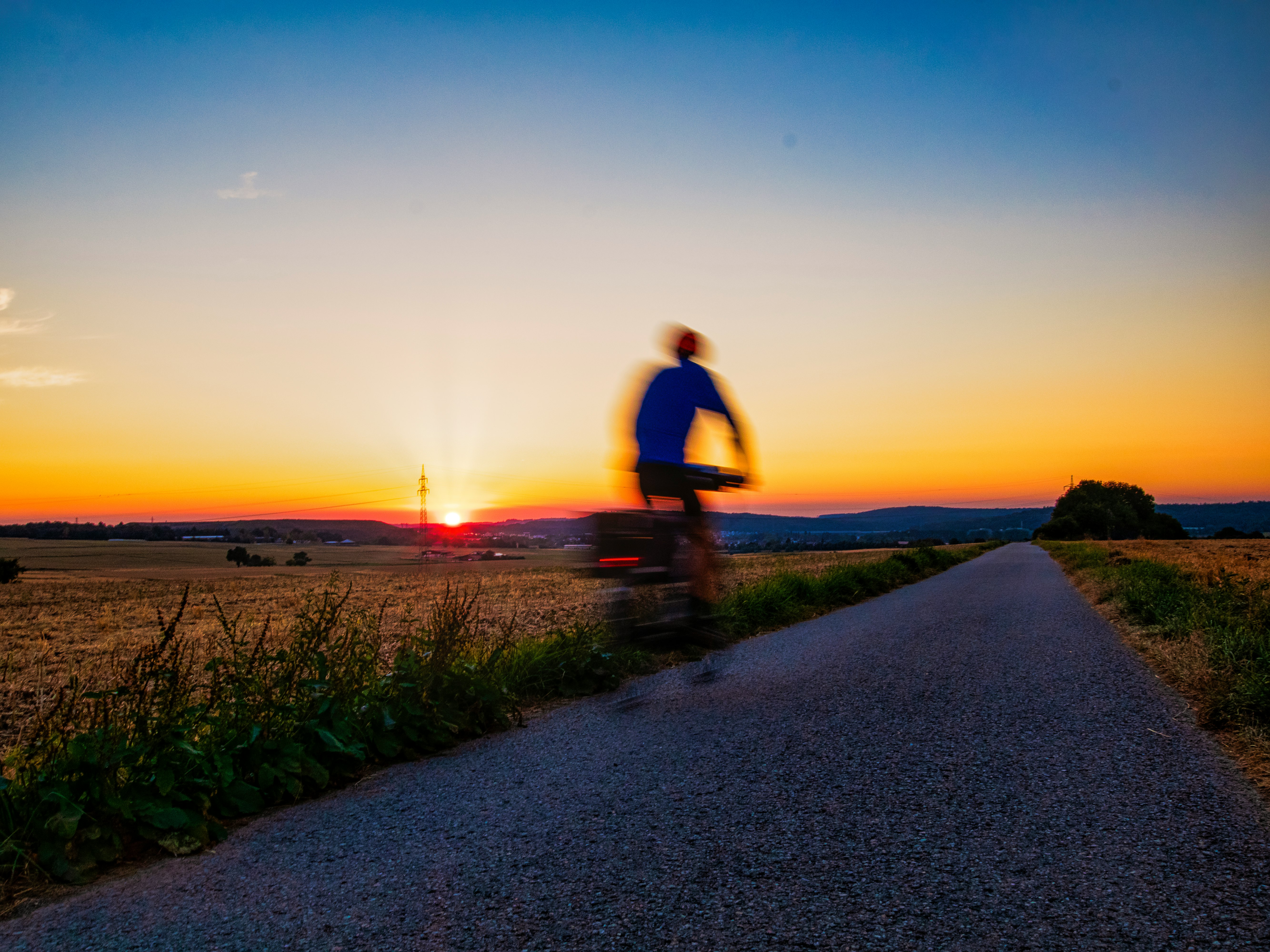 man in black t-shirt and black pants walking on gray concrete road during sunset